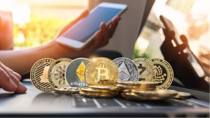 hot cryptos to buy: Various cryptocurrency coins are on a computer in front of someone holding a phone. cryptos for huge profits