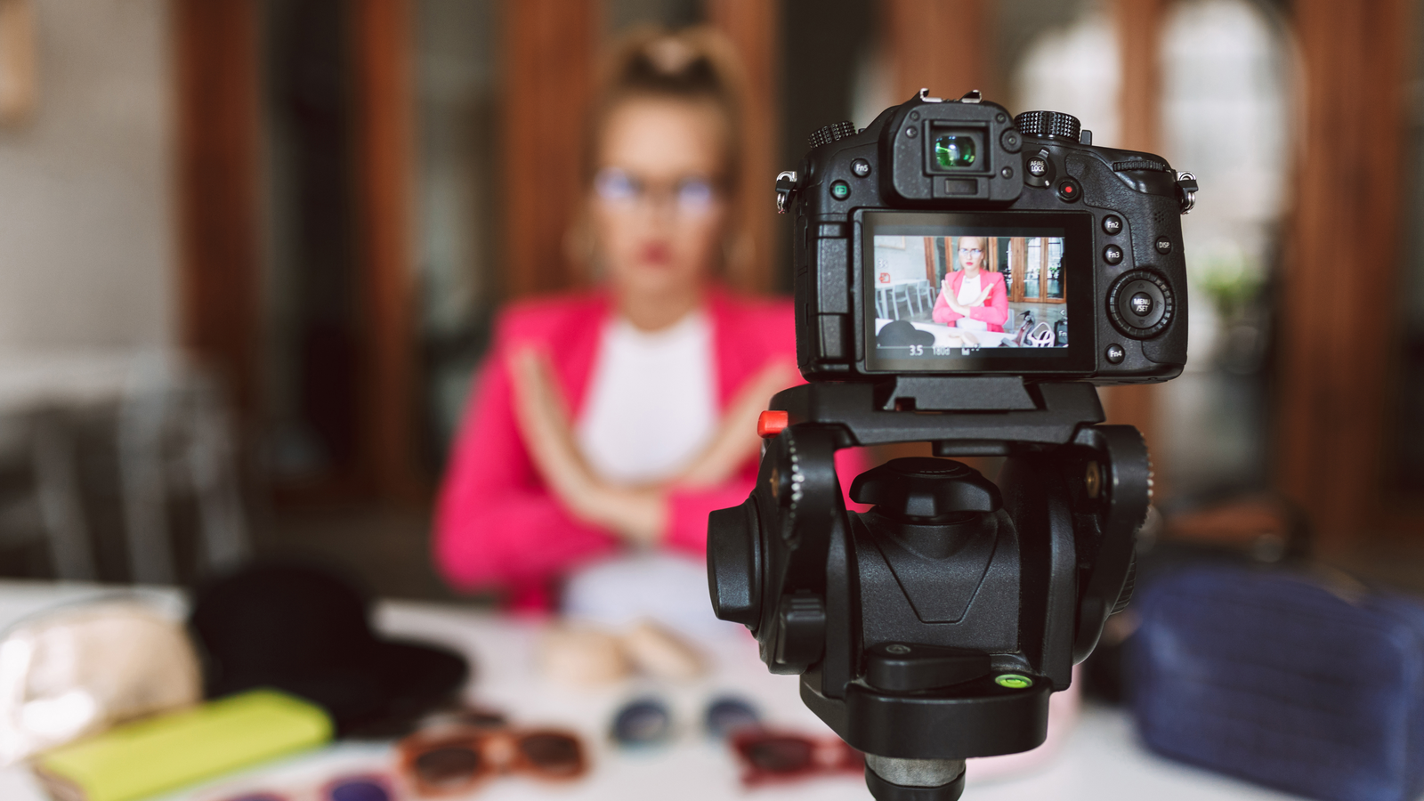MVLA Stock. A woman in a pink jacket sits at a table inside while filming herself on camera