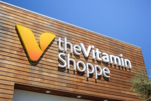 An image of The Vitamin Shoppe logo displayed on a wooden storefront