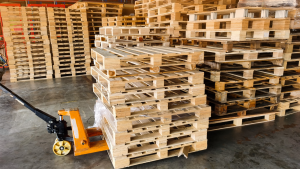 A yellow or orange hand-truck is picking up pallets in a warehouse full of pallets