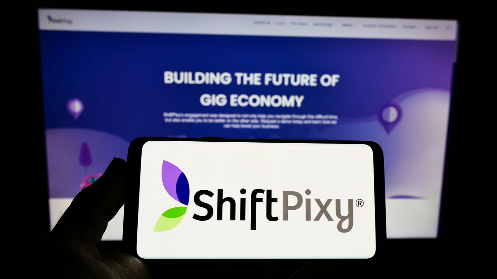 ShiftPixy (PIXY) logo displayed on a smartphone screen with company website on computer monitor behind smartphone