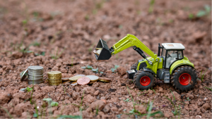 Closeup Of Small green Agricultural Toy Tractor loading money coins, Icon Farmer Machinery, Agriculture Business Concept (Harvest Finance)