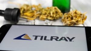 Closeup of mobile phone screen with logo lettering of cannabinoid company tilray cannabis, blurred marijuana and pipette background representing TLRY stock.