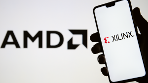 XILINX logo seen on the silhouette of smartphone in a hand and blurred AMD blurred logo on the background.