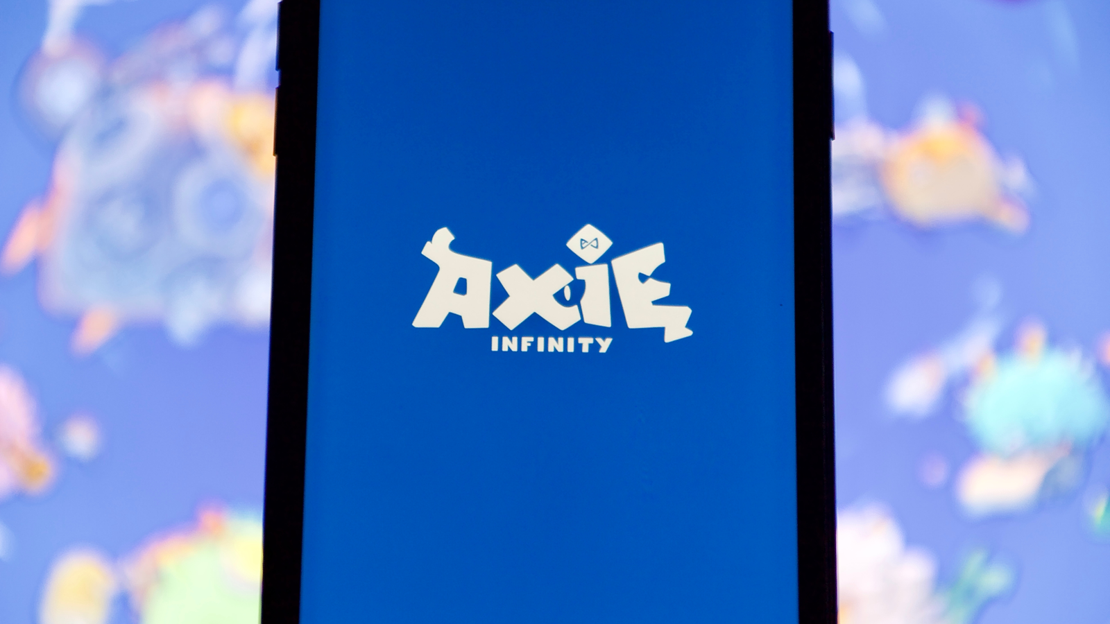 The logo for Axie Infinity (AXS) is displayed on a cellphone screen representing Axie Infinity Price Predictions.