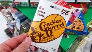 Cracker Barrel gift card in a hand over a shelves with different giftcards