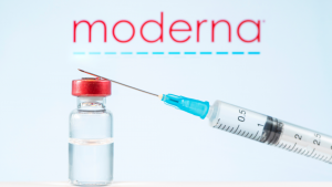 red text reads "moderna" on a light blue background. there is a bottle of liquid vaccine next to a medical needle