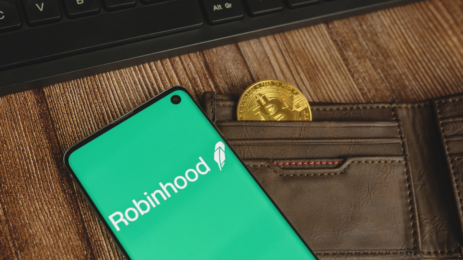 hood stock: An image of a wallet with a coin in it, a cellphone on top depicting Robinhood logo