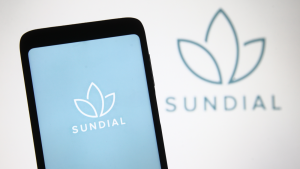 The Sundial Growers logo is on a phone screen with a light blue background in front of the sundial logo on a white background. SNDL stock