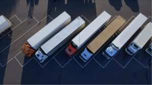 trucking stocks Aerial Top View of White Semi Truck with Cargo Trailer Parking with Other Trucks on Special Parking Lot.