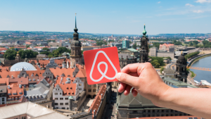 meone holds the Airbnb logo in front of Dresden, Germany landscape. ABNB stock.