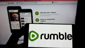 Person holding cellphone with logo of Canadian video platform company Rumble (RUM) Inc. on screen in front of business webpage. CFVI