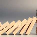 A photo of a series of dominos falling and leaning on each other, with the last one held up by a stack of quarters that stays upright.