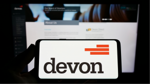 An image of a hand holding a smartphone displaying the Devon Energy Corporation logo in front of a computer screen