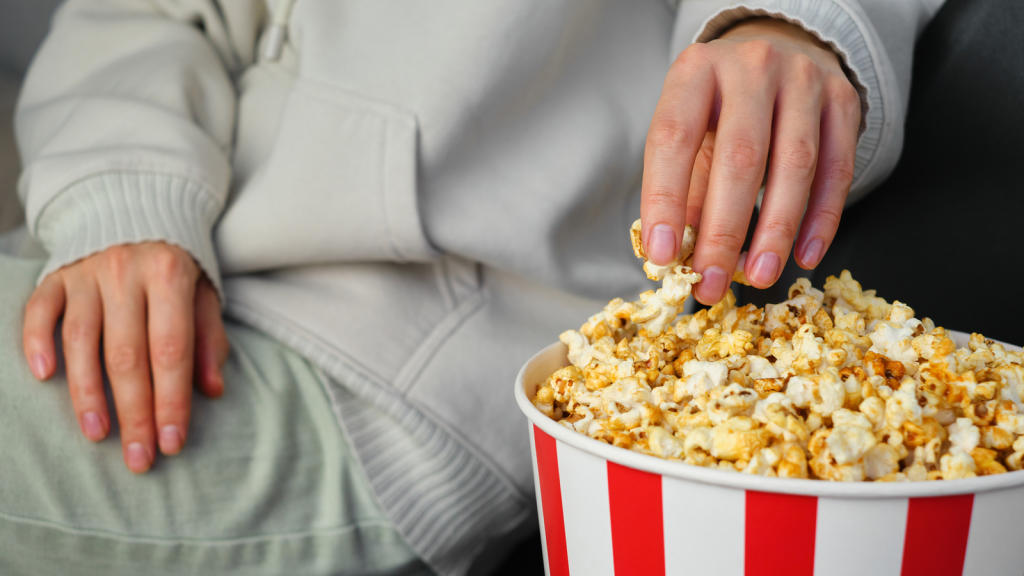 A hand dipping into a bowl of popcorn, representing entertainment industry; eating while enjoying entertainment. Entertainment stocks.
