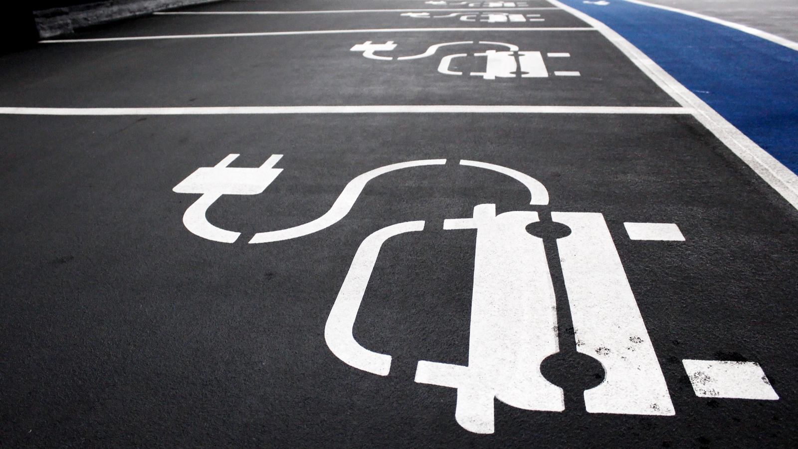 An image of parking spaces in a parking lot with EV charging icons painted on the ground