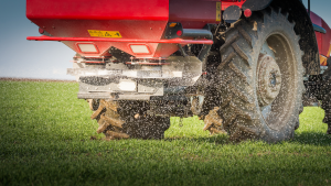 A tractor spreading fertilizer over a farm field representing Fertilizer Shortage 2022.