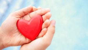 hands holding a red heart on a blue background symbolizing health