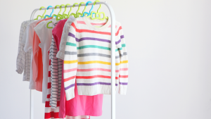 A photo of children's clothing hanging from hangers on a movable rack in a white room.