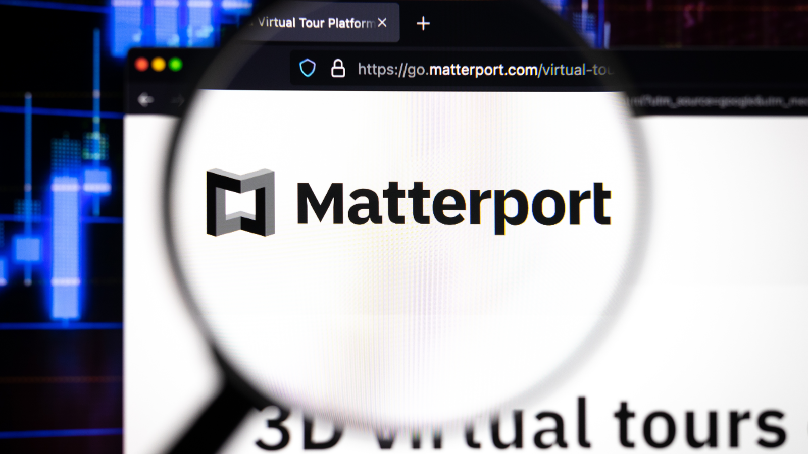 Matterport company logo on a website with blurry stock market developments in the background, seen on a computer screen through a magnifying glass. MTTR stock.