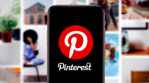 Smart phone with the Pinterest (PINS) logo in front of blurred out pinterest post pictures