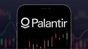 背景に一連の株価チャートが表示されたスマートフォン内の Palantir (PLTR) のロゴ。