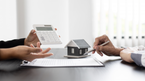 An image of two people with a housing contract, hands holding a pen, hands holding a calculator with a house in the background