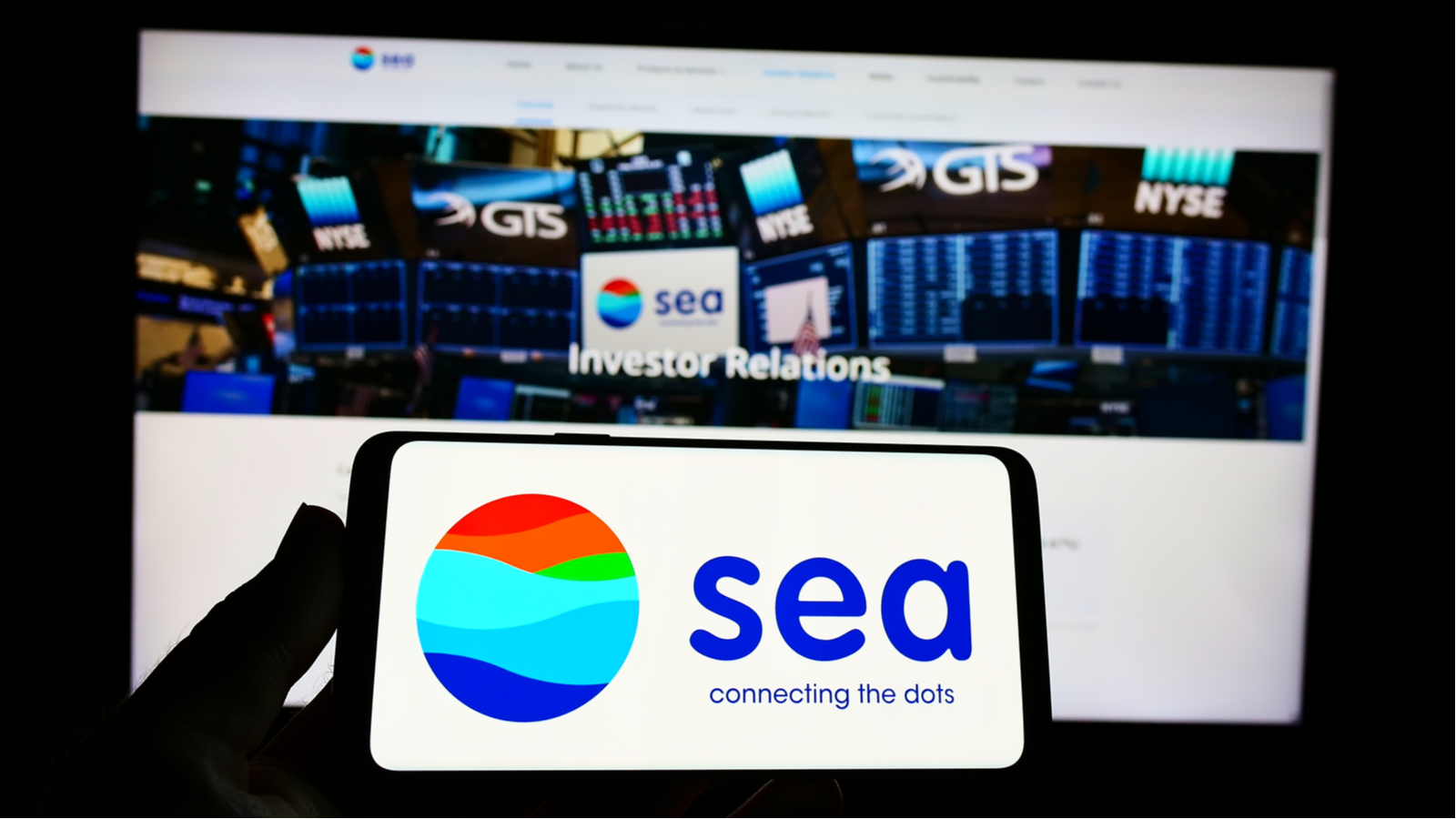 Person holding cellphone with logo of Singaporean technology conglomerate Sea Ltd on screen in front of business webpage Focus on phone display. SE stock