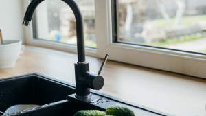A photo of a black faucet and sink next to a window.