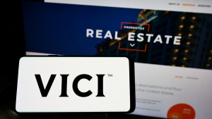 Person holding mobile phone with logo of American real estate company Vici Properties Inc. on screen in front of web page. VICI stock.
