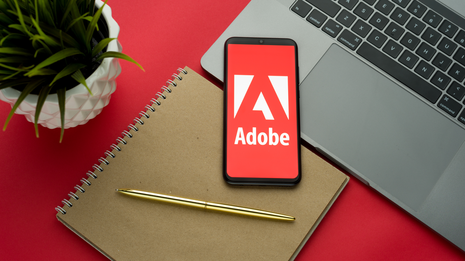 Adobe logo on the smartphone screen is placed on the Apple macbook keyboard on red desk background. ADBE stock.