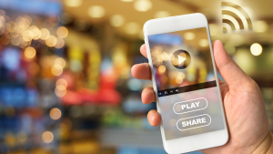 Woman holding smartphone in hand against blurred bokeh of store background. VDO advertising concept, April brings video marketing, social media and real estate together