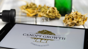 Closeup of mobile phone screen with logo lettering of cannabinoid company canopy growth cannabis, blurred marijuana in the background. CGC stock.