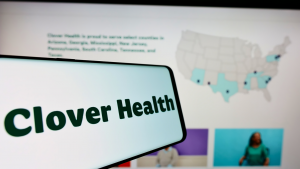 Clover Health のロゴが、コンピューター画面の前の電話画面に表示され、サービスが提供される場所の地図が表示されます。 CLOV株。