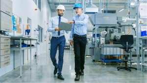 Rear view of project manager holding laptop and discussing product details with chief engineer while they walk through modern factory.  FR rents these spaces in the United States