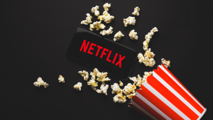 画面に Netflix のロゴが表示されたスマートフォンが、ポップコーンを広げたポップコーンの容器の横に置かれている画像