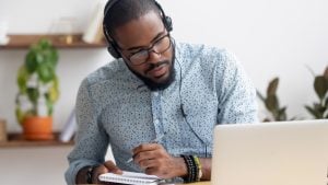 Man in headphones writing notes in notebook while watching webinar video course