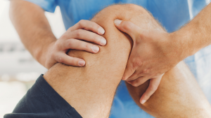 Physiotherapist giving treatment to patient's leg. Therapist in blue uniform. Osteopathy, chiropractic leg adjustment. Orthopedic therapy. ATIP stick.