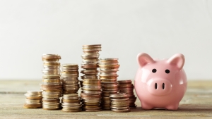 Piggy bank on a wooden table with stacks of coins next to it. Cryptos to Buy