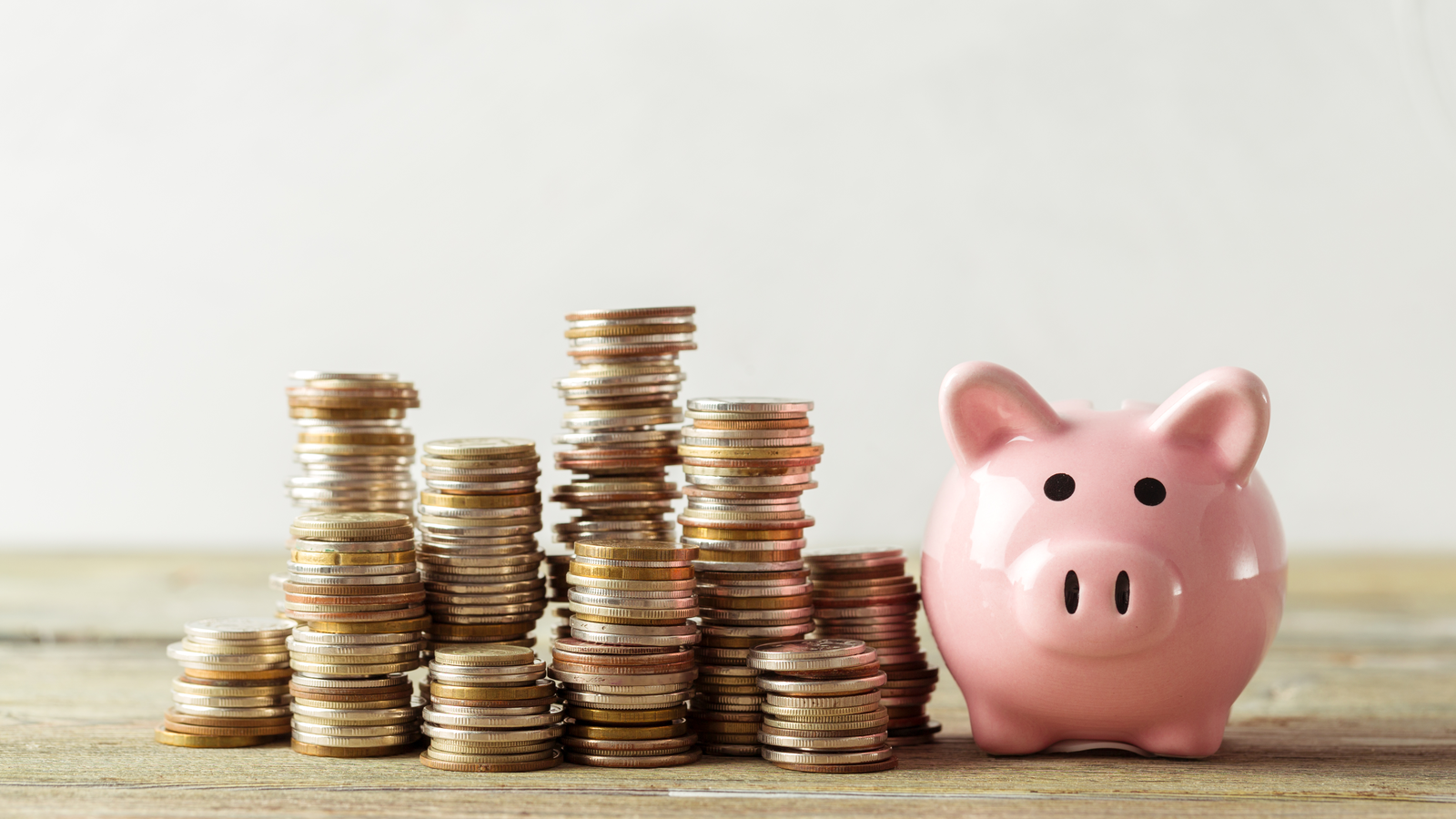 Piggy bank on a wooden table with stacks of coins next to it.