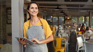 Portrait of a happy waitress standing at restaurant entrance holding digital tablet. Restaurant.