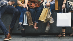 Friends sit on a ledge with shopping bags after shopping retail stores.