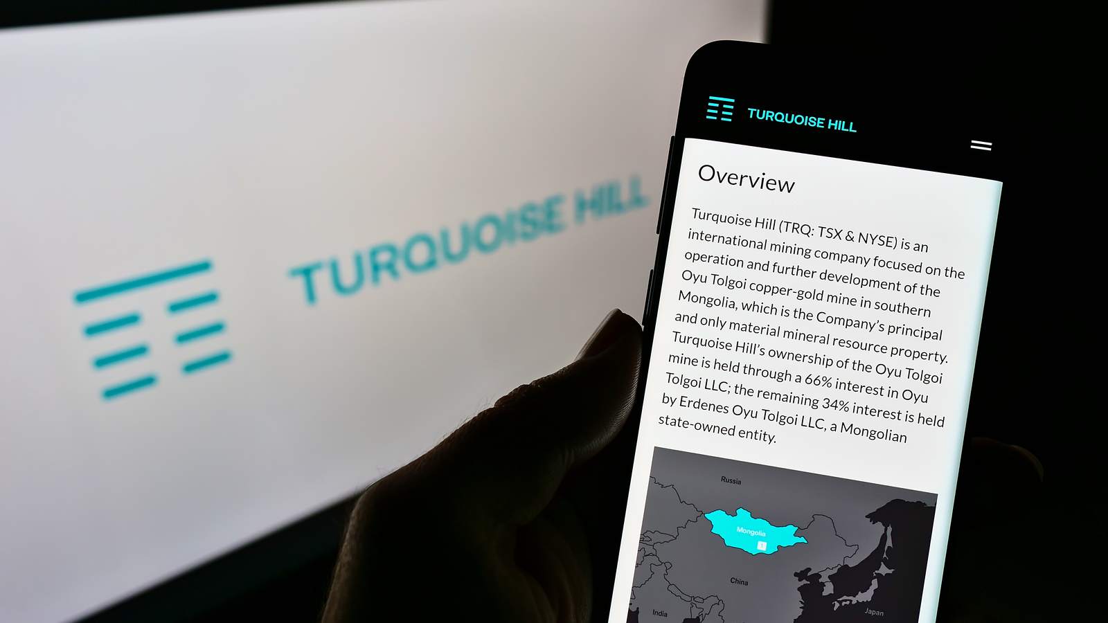 Person holding cellphone with website of Canadian mining company Turquoise Hill Resources Ltd on screen in front of logo. Focus on phone display. TRQ stock.
