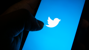 Twitter (TWTR Stock) logo displayed on a smartphone screen with a hand ready to use the app