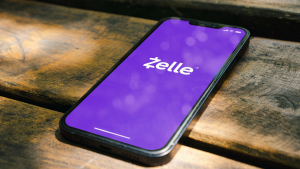 Zelle app logo displayed on a smartphone placed on a wooden table with sunlight shining on phone