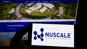 A hand in silhouette holds up a phone displaying the logo for Nuscale (SMR) in front of a display showing the company's website.