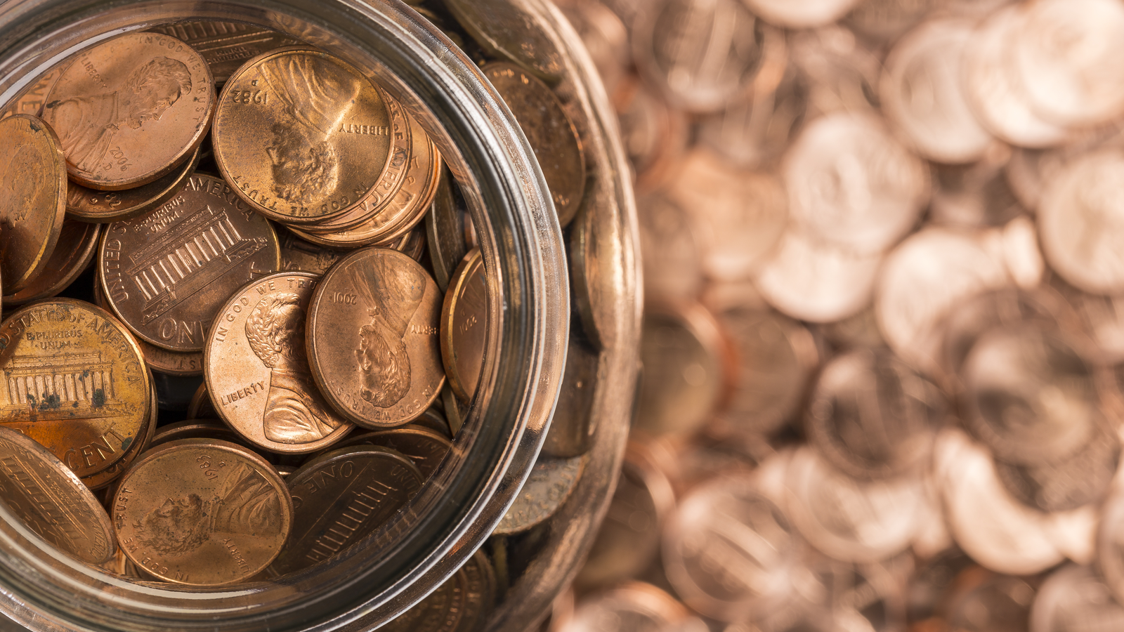 Pennies in a jar on top of a background of pennies. Pennies. Cheap stocks.