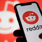 Reddit Layoffs. Phone showing Reddit logo on screen in front of blurred background with reddit logo. Reddit IPO.