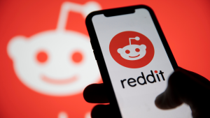 Phone showing Reddit logo on screen in front of blurred background with reddit logo. Reddit IPO.