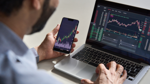 Businessman analyzing stocks to trade at his computer and on his phone